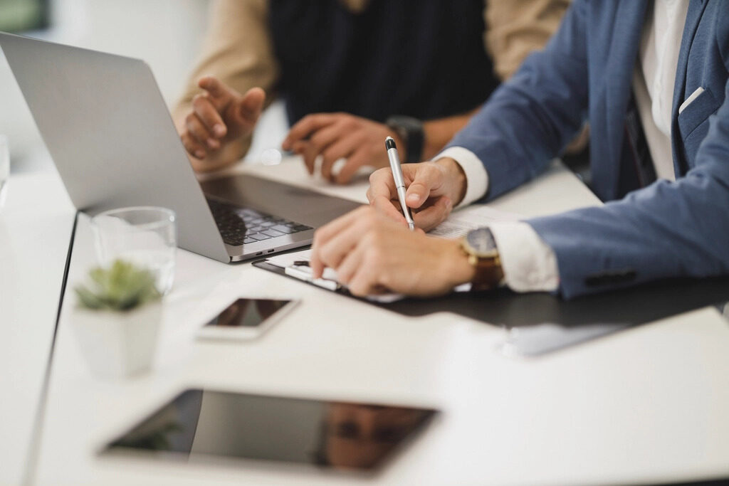 Two professionals reviewing documents and taking notes beside a laptop at a meeting table